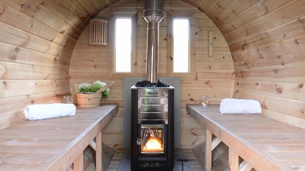 A cozy wooden cabin with a central wood stove, benches, and a small window. - B&B De Witte Merel Deluxe (Beringen)