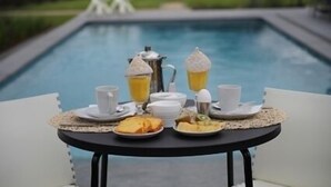 A breakfast setup with a table by a pool, including a pitcher, cups, and plates of food. - B&B De Witte Merel Deluxe (Beringen)