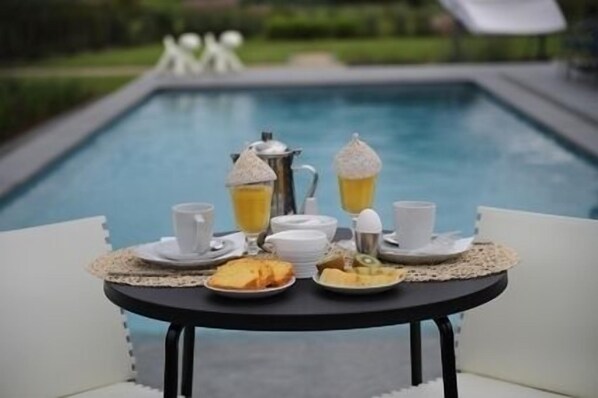 A breakfast setup with a table by a pool, including a pitcher, cups, and plates of food.