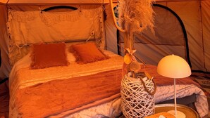 A cozy tent interior with a bed, a hanging mirror, a lamp, and a bedside table with a tissue box. - B&B De Witte Merel Deluxe (Beringen)
