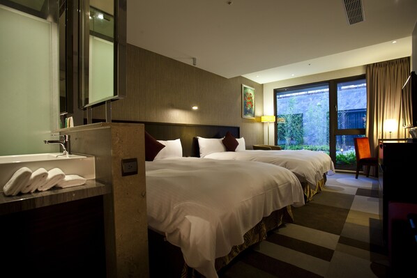 A hotel room with two beds, a large window, a bathroom with a sink and towels, and a desk with a chair.
