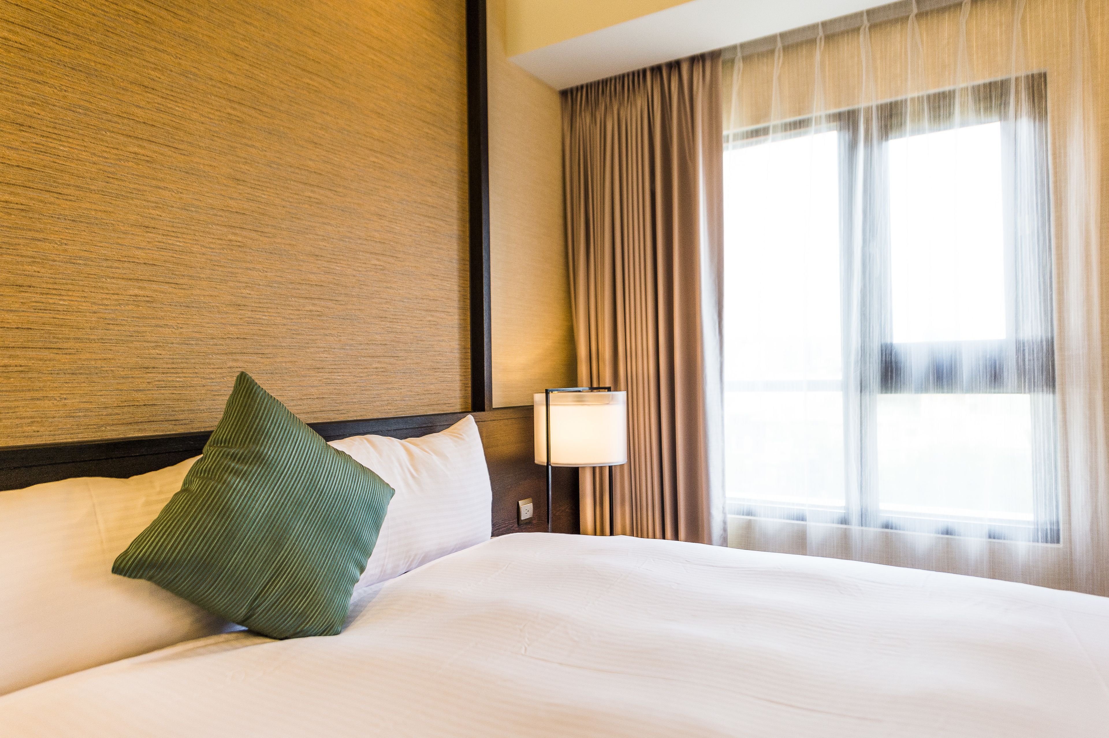 Una habitación de hotel con una cama bien hecha, una lámpara y un ventanal con cortinas.