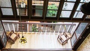 A high-ceilinged room with a wooden floor, a hanging light fixture, and a view through a window with a lattice design.