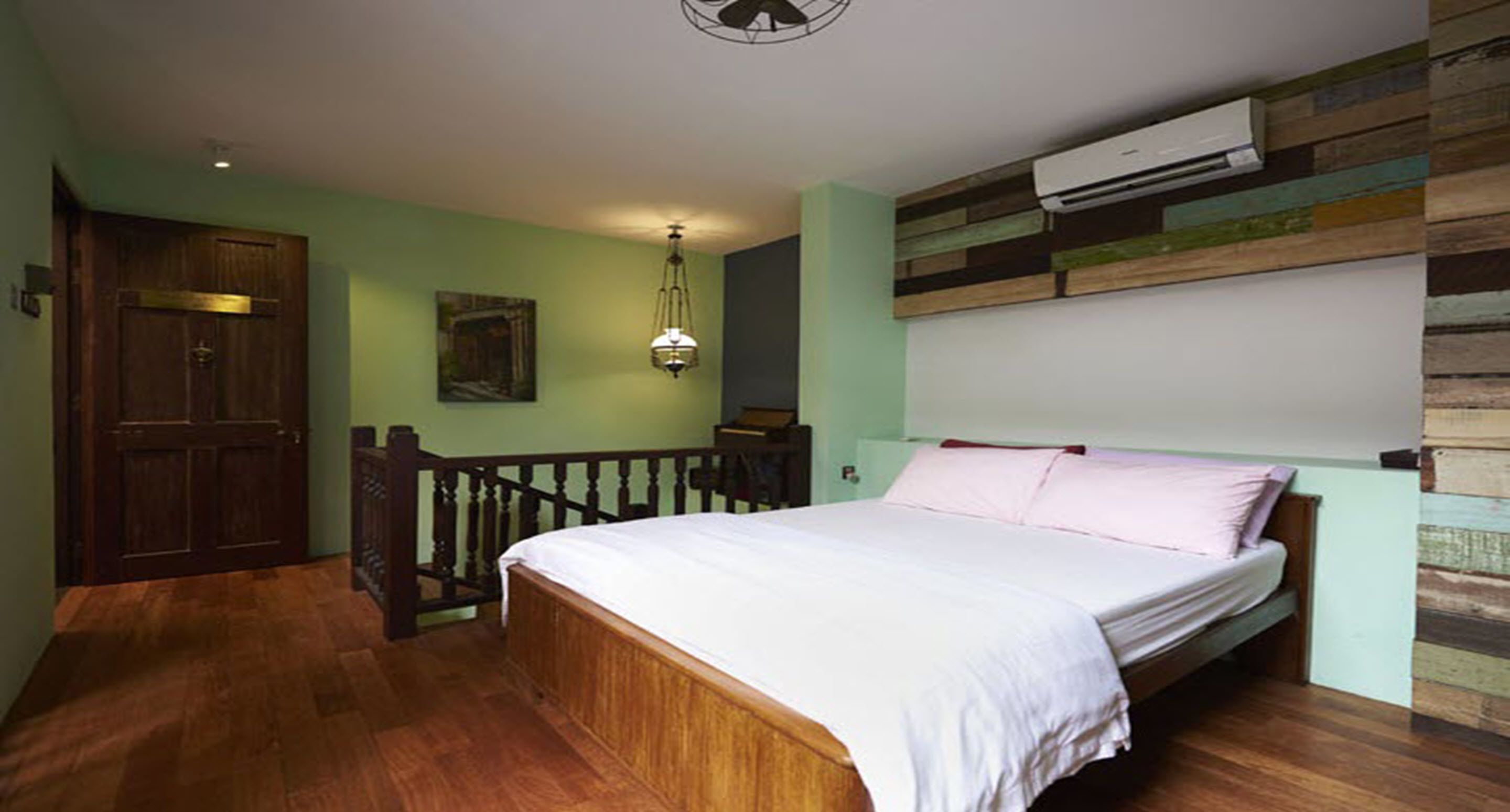 Un dormitorio con una cama y barandilla de madera, un ventilador de techo y aire acondicionado instalado en la pared.