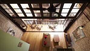 A room with a high ceiling, wooden beams, and a skylight. There is a sofa and a small table with chairs.