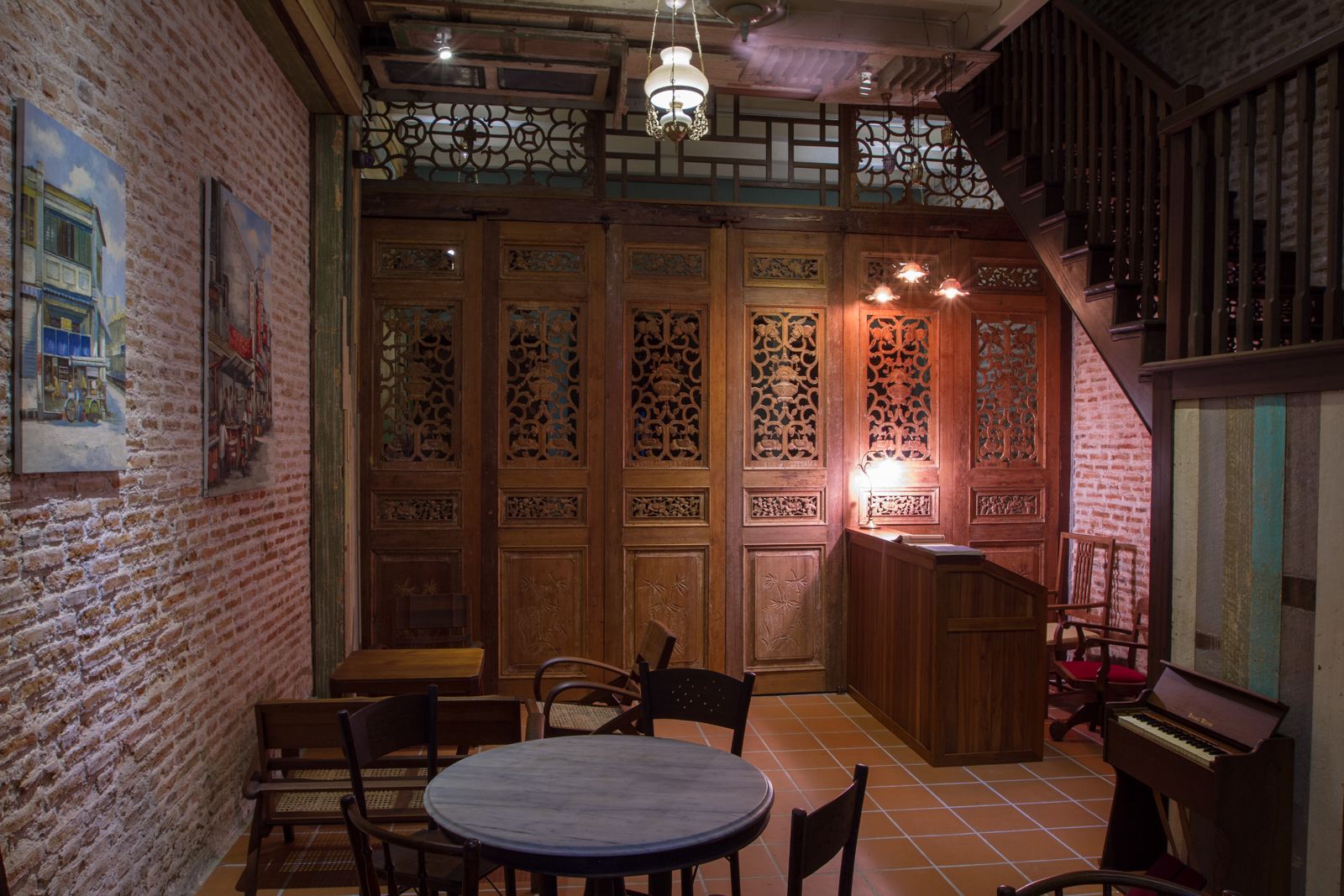 A traditional interior with a brick wall, wooden doors with intricate carvings, a piano, and a round table with chairs.