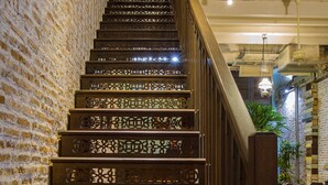 A wooden staircase with intricate carvings, leading to a room with a brick wall and a tiled floor.