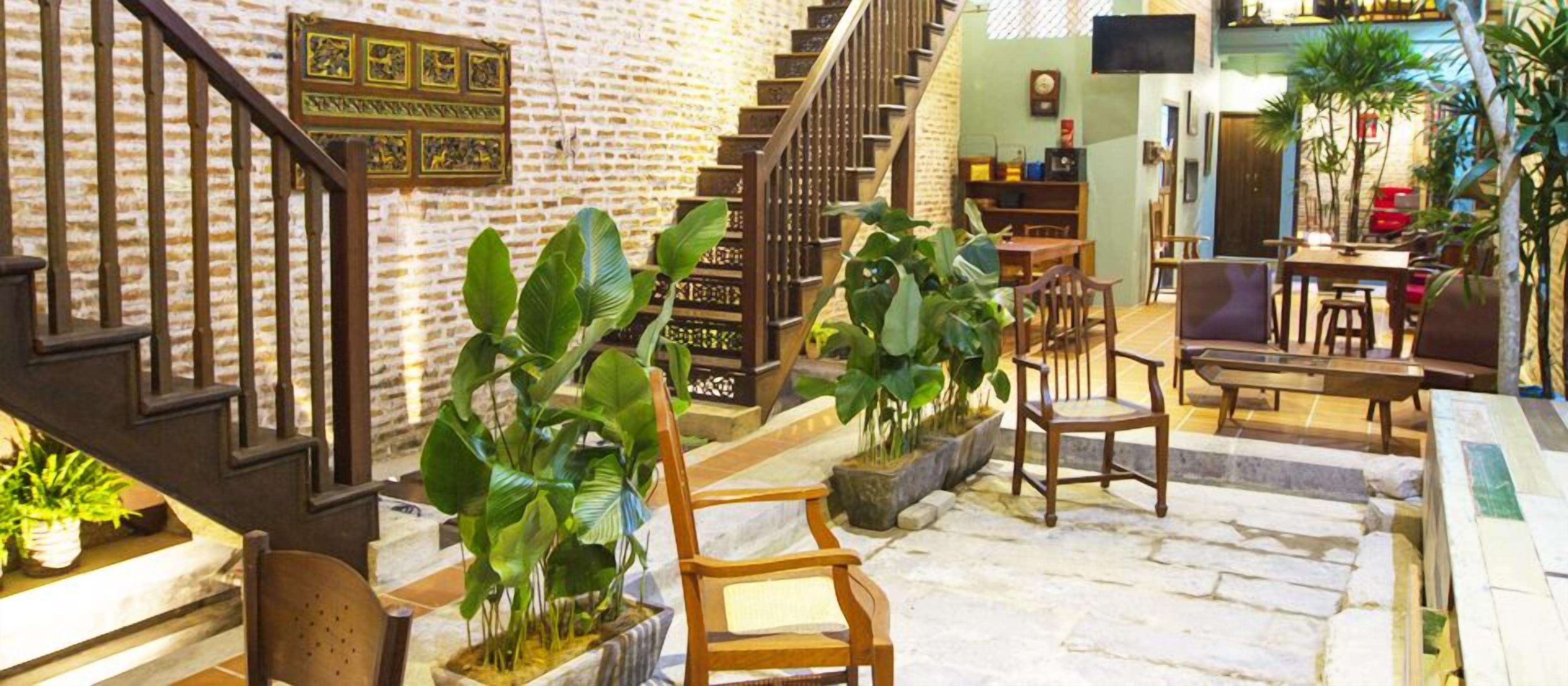 Un hall d’entrée spacieux avec un escalier, des chaises en bois et des plantes en pot.