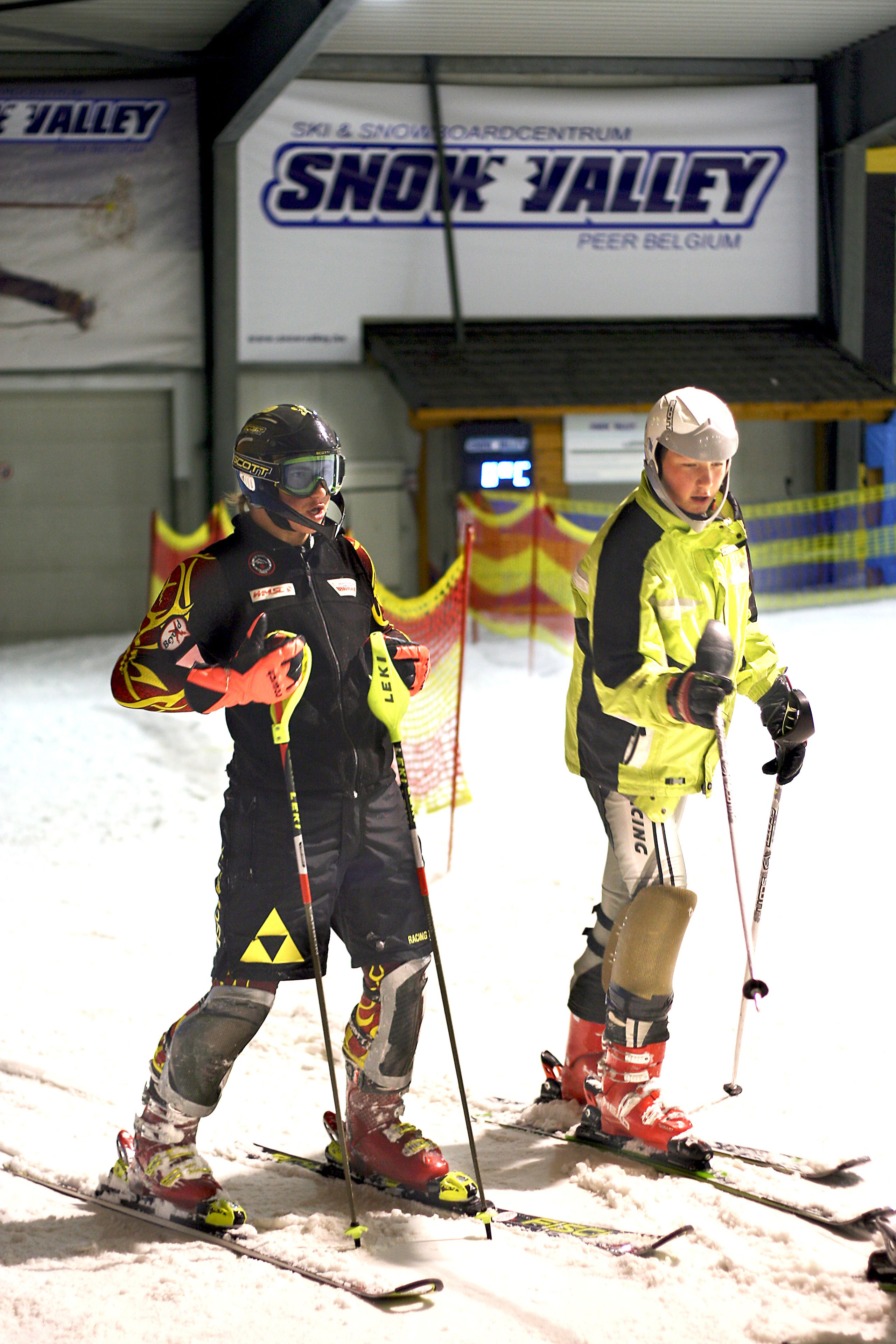 Two skiers in an indoor skiing facility with a sign reading "SNOK VALLEY".