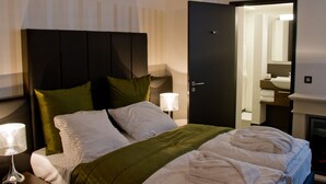 Et hotelværelse med seng, natbord, lampe, dør og spejl.