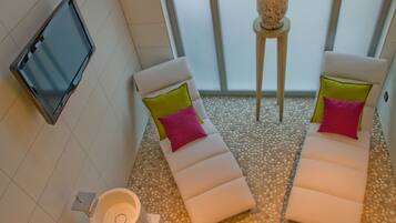 Una sala de spa con dos sillones reclinables, una mesita con una planta, un televisor en la pared y un suelo de baldosas.