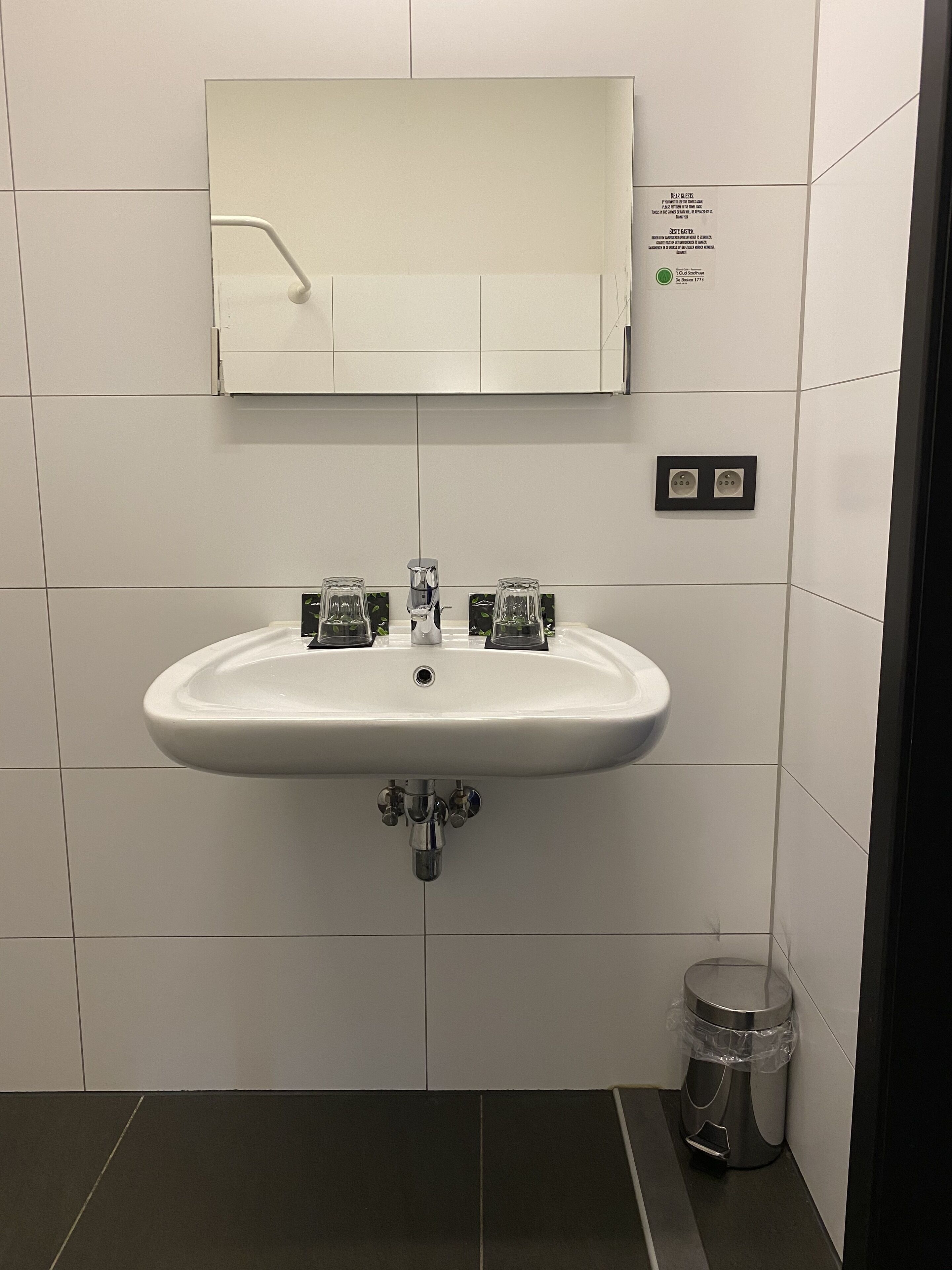 Une salle de bain avec un lavabo blanc, un miroir et une poubelle.