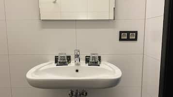 Un baño con lavamanos blanco, espejo y basurero.