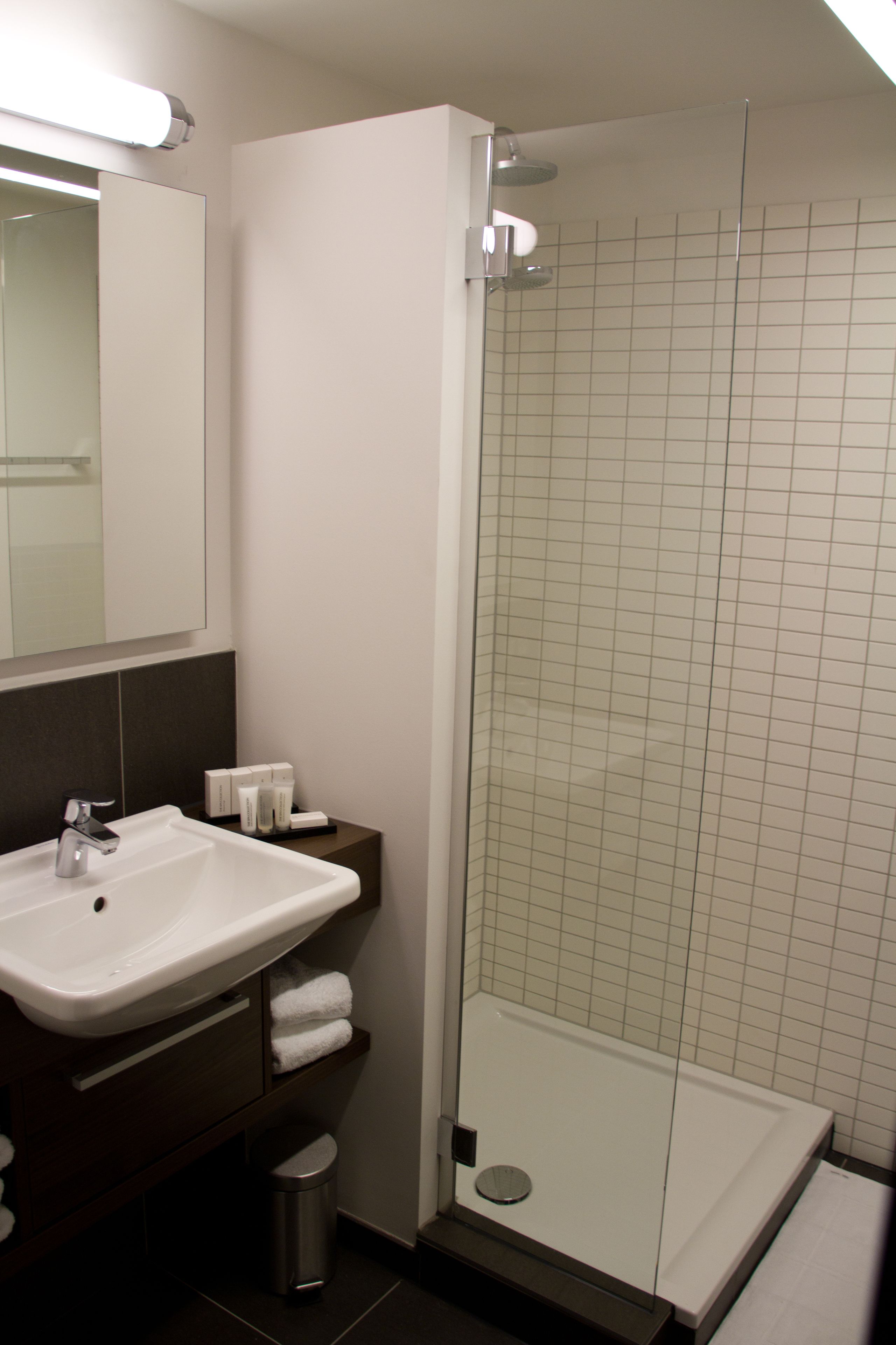 A modern bathroom with a white sink, mirror, and glass-enclosed shower.