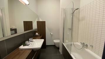 Un baño moderno con ducha envuelta en vidrio, un lavabo blanco y un mueble de tocador de madera.