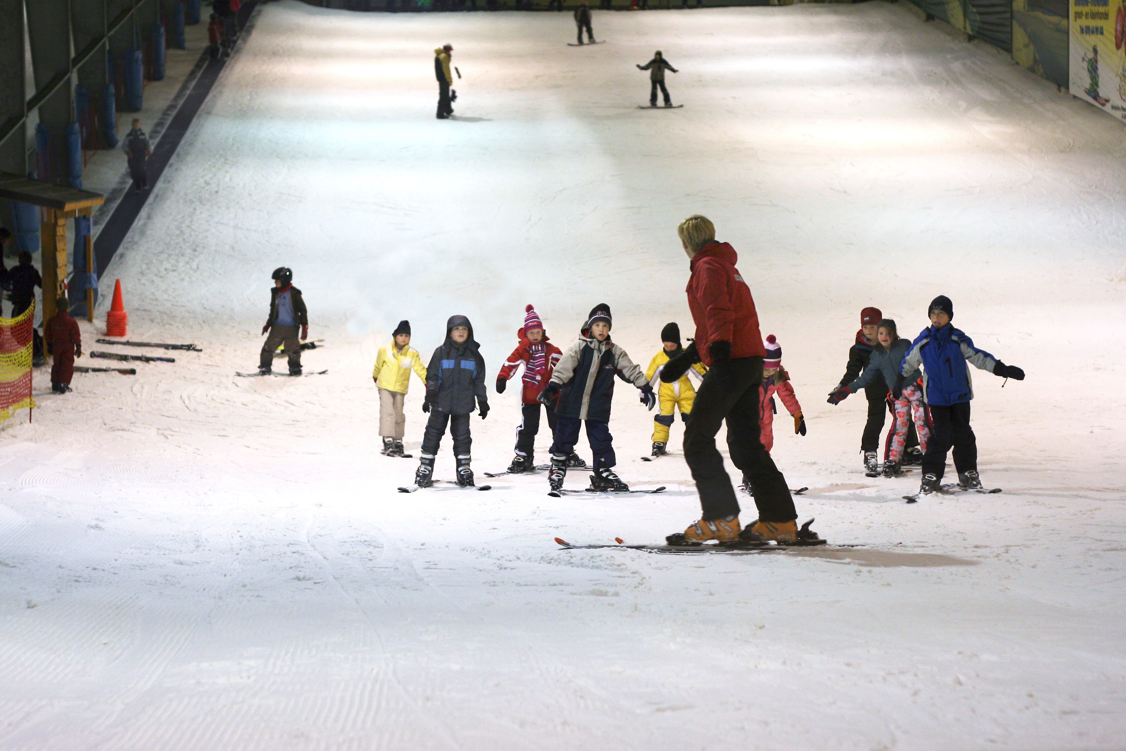 A ski slope with people skiing and a person in a red jacket standing in the middle.