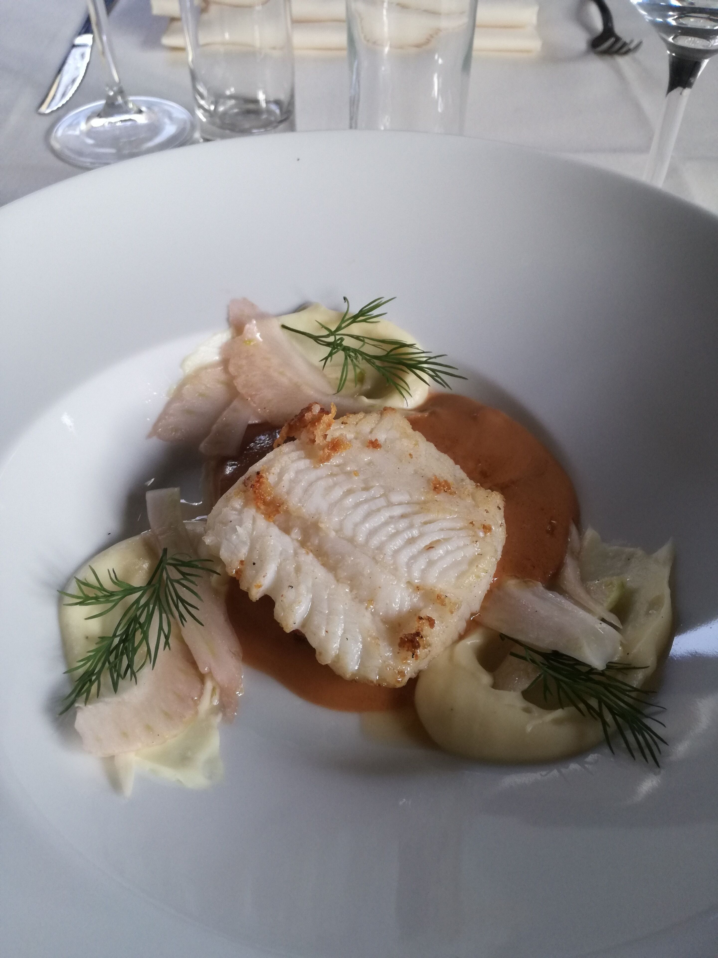 A white plate with a piece of fish, some vegetables, and a sauce.