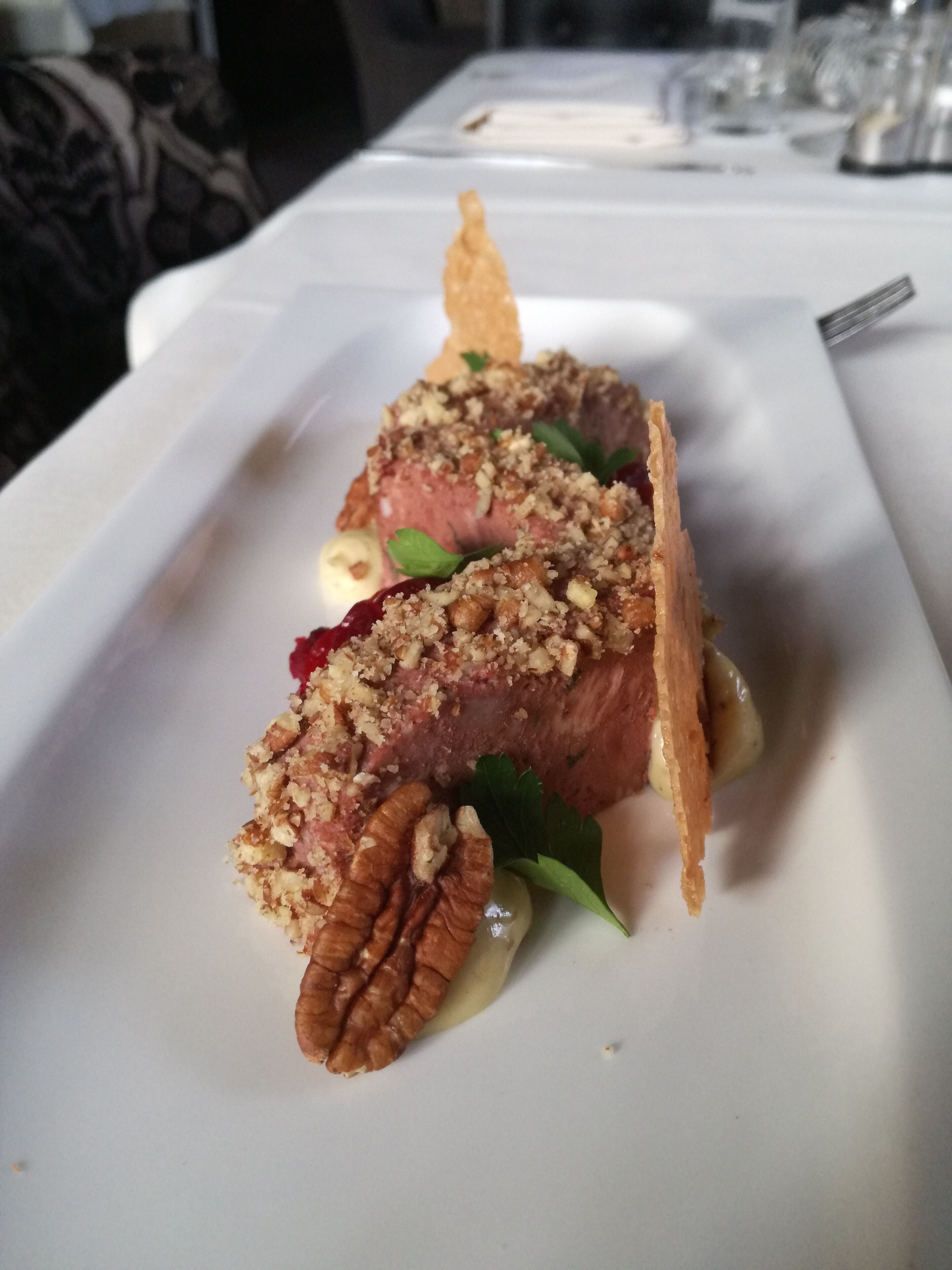 A plated dish with a meat centerpiece, garnishes, and a side of sauce.