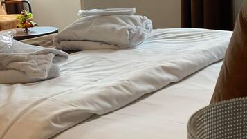 A neatly made bed with white linens and pillows, a bedside table with a fruit bowl, and a window with curtains.