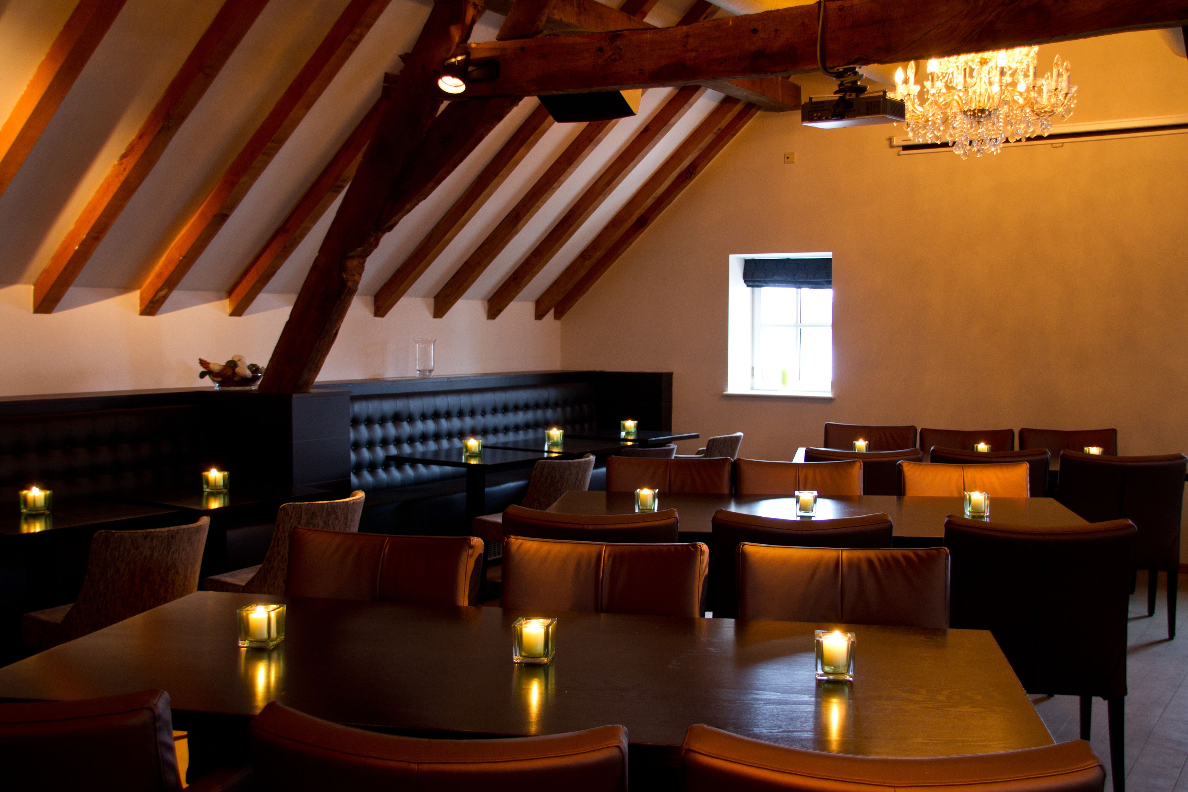 Un restaurant avec des poutres en bois, des tables éclairées à la bougie et un lustre.