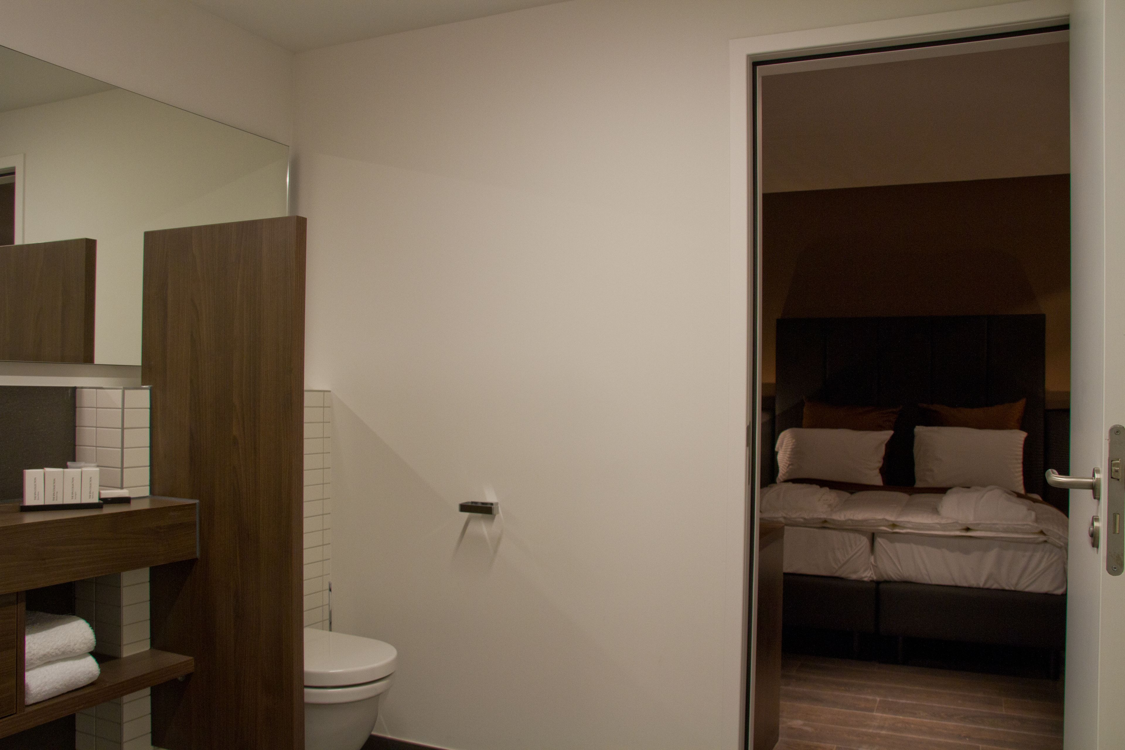 Een hotelkamer met een houten opbergmeubel, toilet en een bed met kussens.