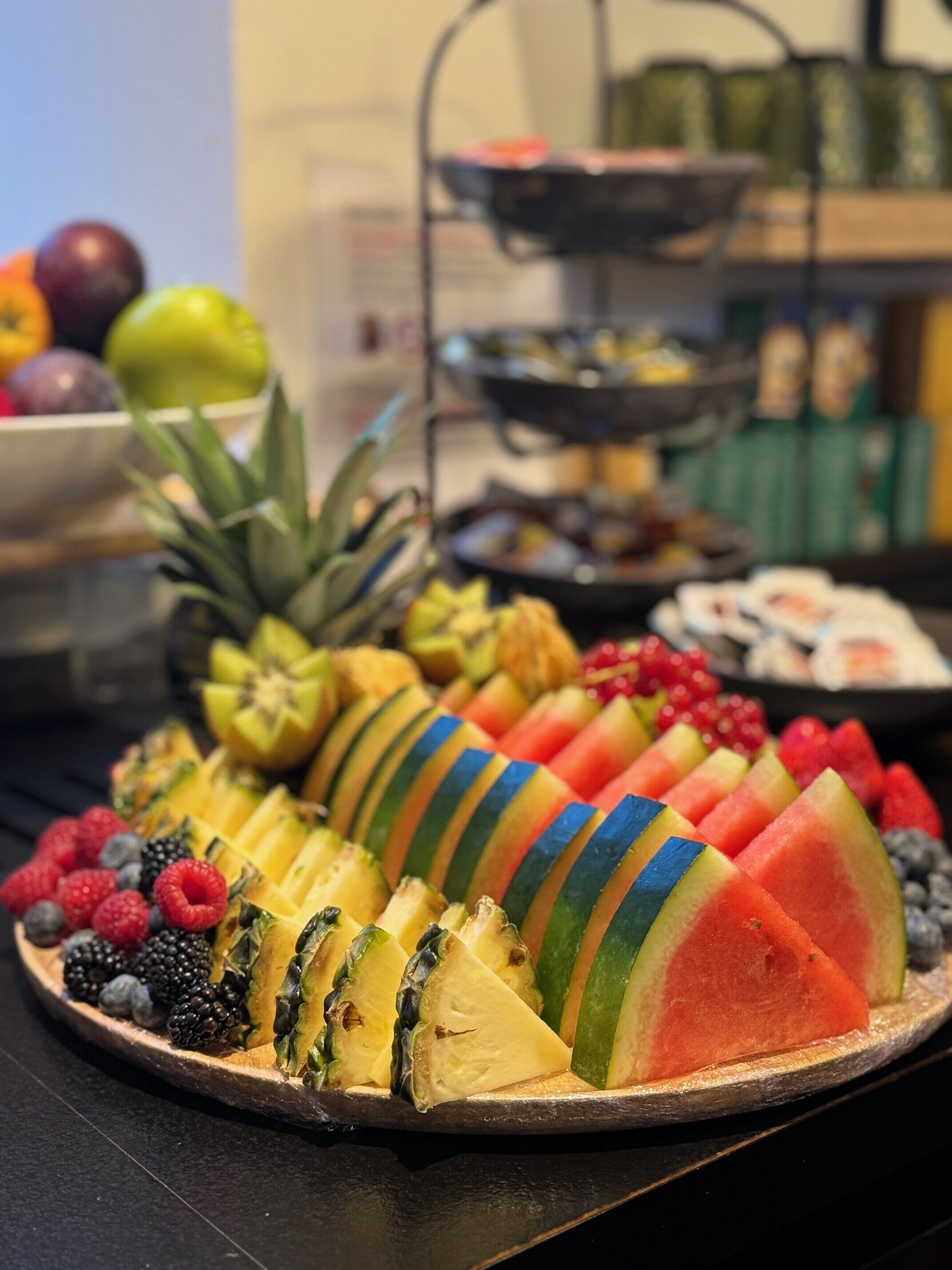 A fruit platter with pineapple, watermelon, and berries on a wooden board.