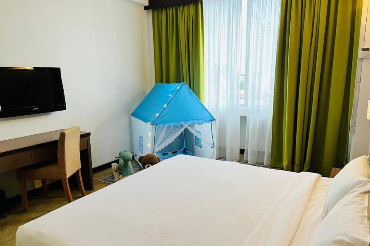 Habitación de hotel con cama, escritorio, televisión, una estructura parecida a una tienda de campaña y cortinas verdes.