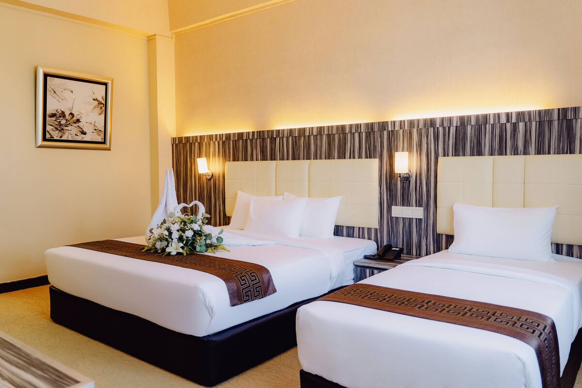Habitación de hotel con dos camas, un cuadro en la pared y una mesita de noche con una lámpara.