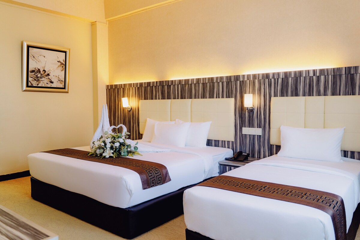 A hotel room with two beds, a framed picture on the wall, and a nightstand with a lamp.