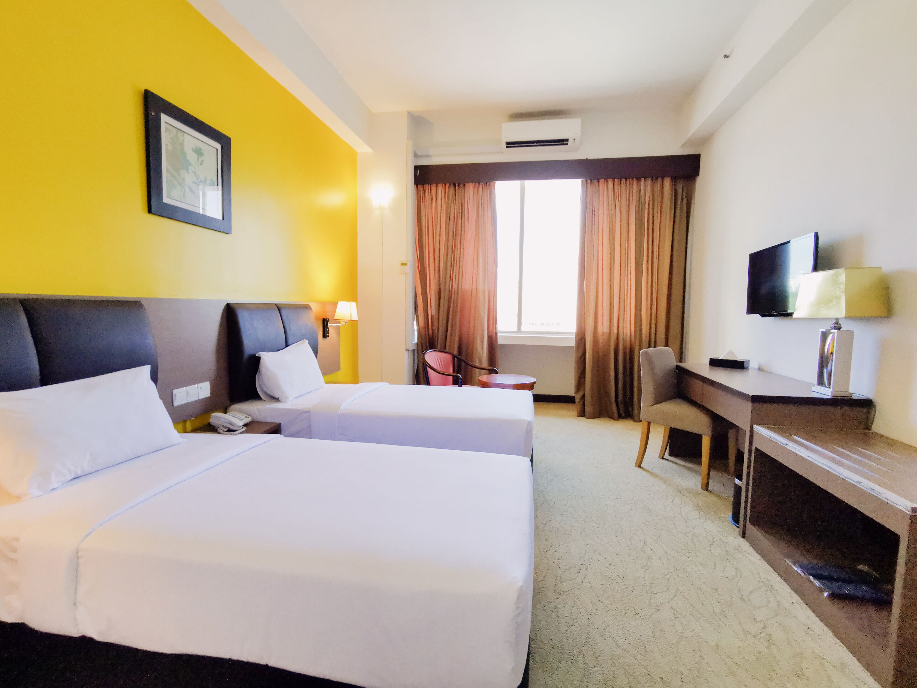 A hotel room with two beds, a desk, a chair, a television, and an air conditioning unit.