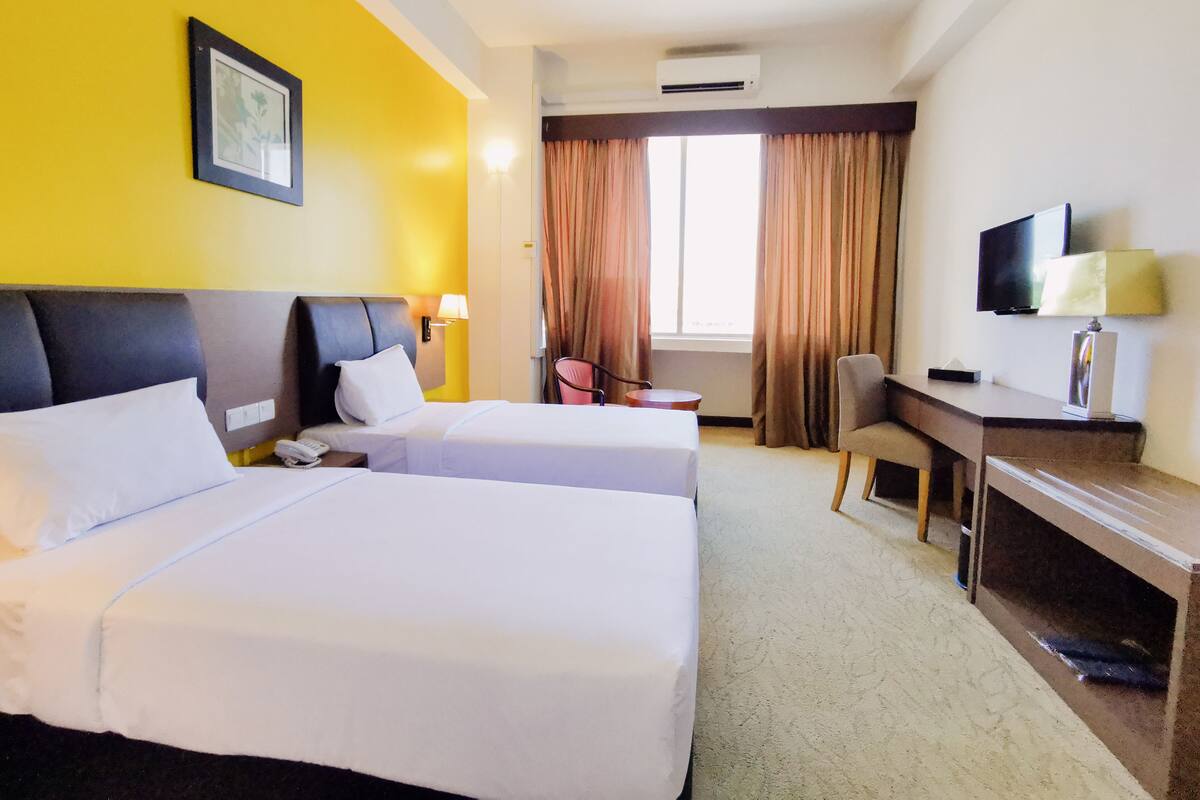 Habitación de hotel con dos camas, un escritorio, una silla, un televisor y un equipo de aire acondicionado.