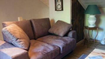 A brown leather sofa with cushions, a small table with a green lamp, and a framed picture on the wall.
