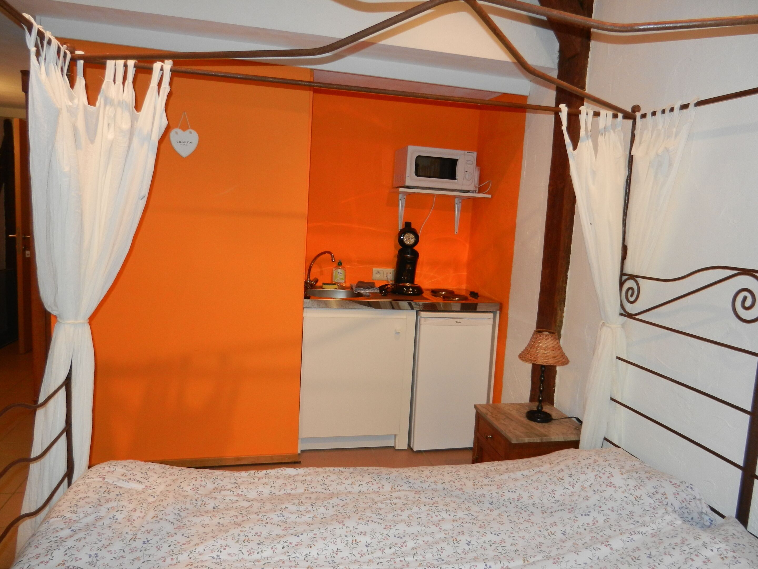 A bedroom with a bed, a small kitchenette, and a window with curtains.