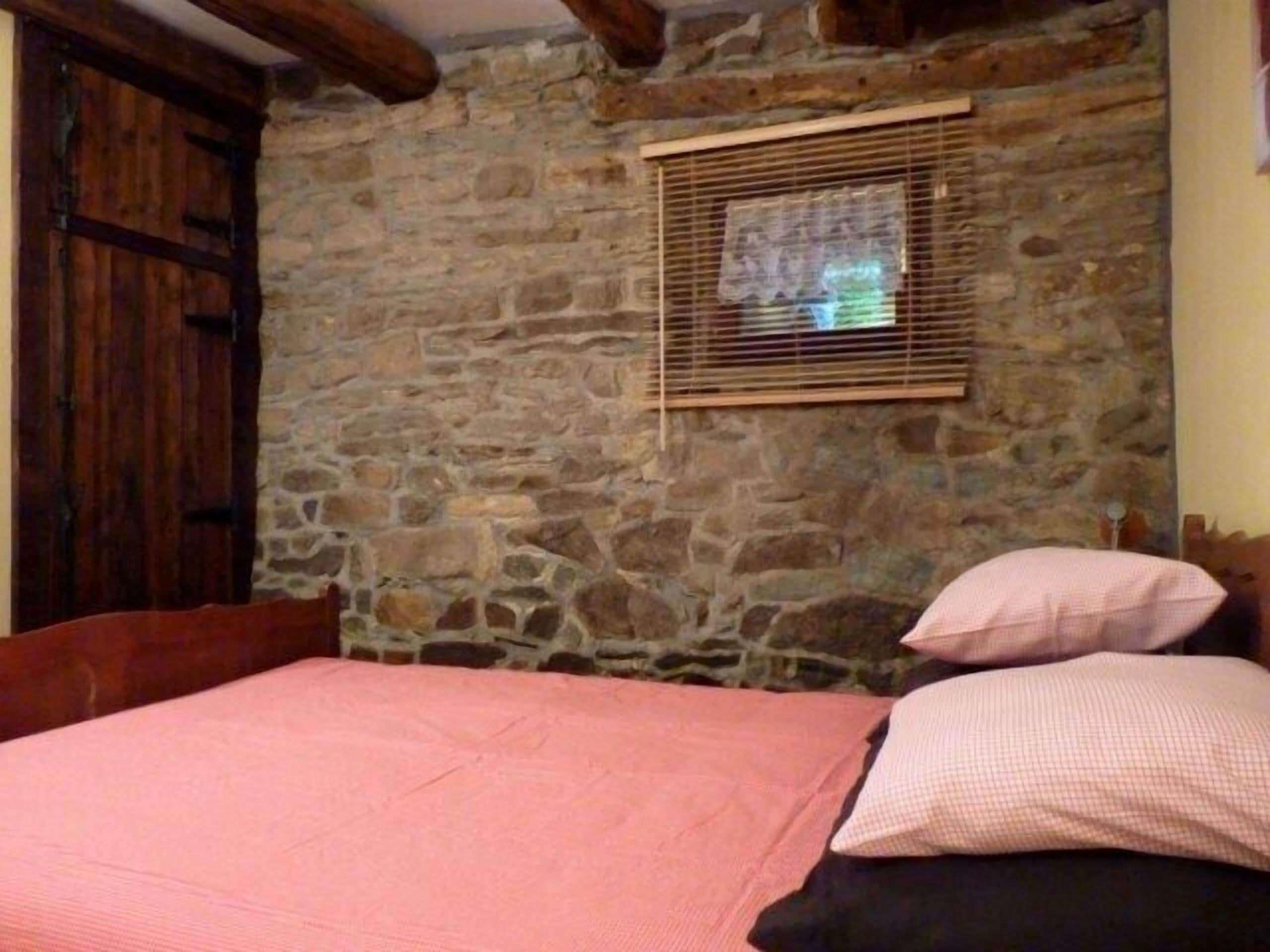 Ein Zimmer mit einer Steinsäule, einer Holztür, einem Fenster mit Jalousien und einem Bett mit rosa Bettwäsche.