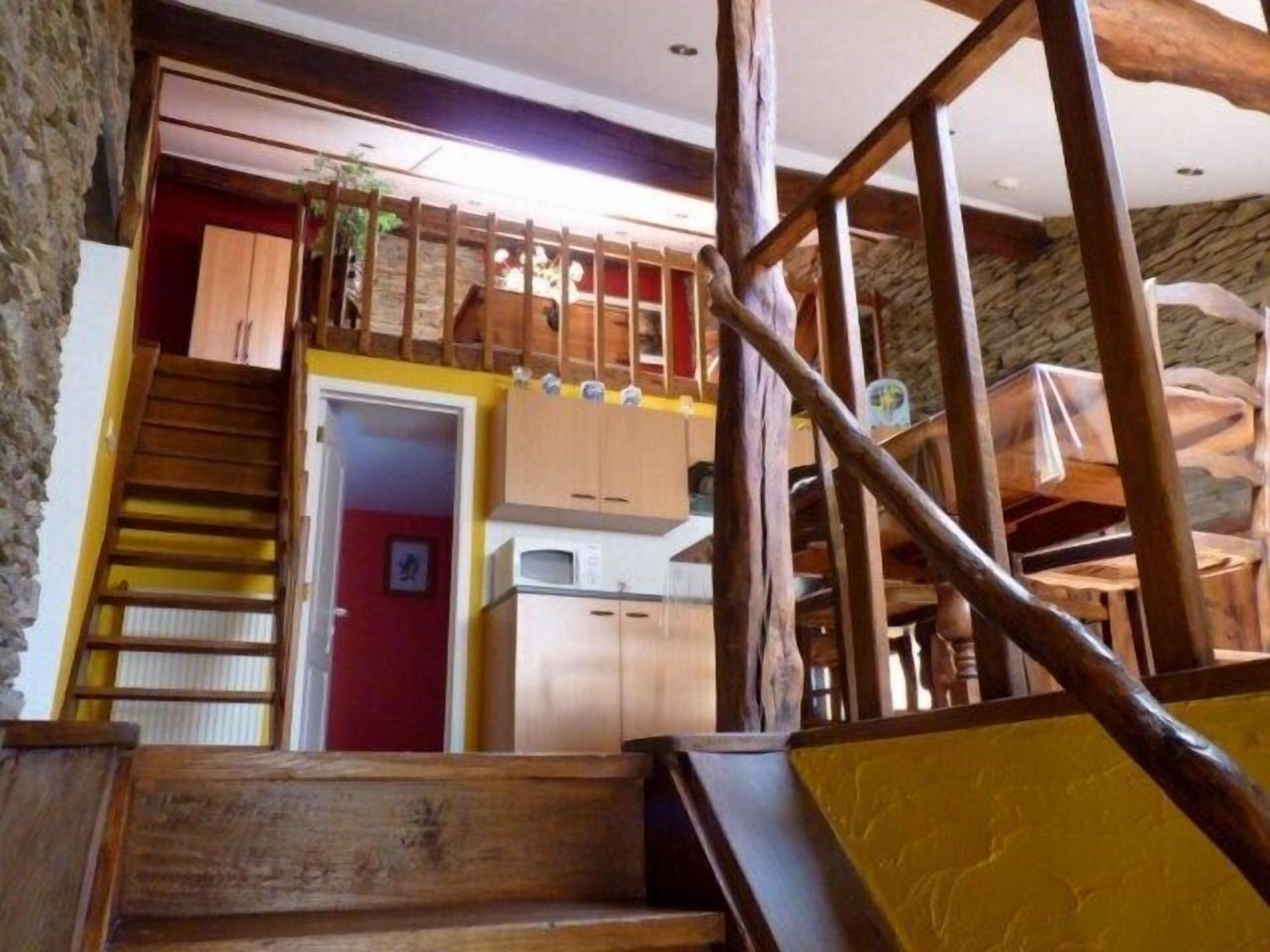 A wooden staircase leading to a lofted area with a kitchen and a red door.