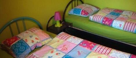 Une petite chambre avec un lit simple, un matelas vert et une couverture aux couleurs vives.