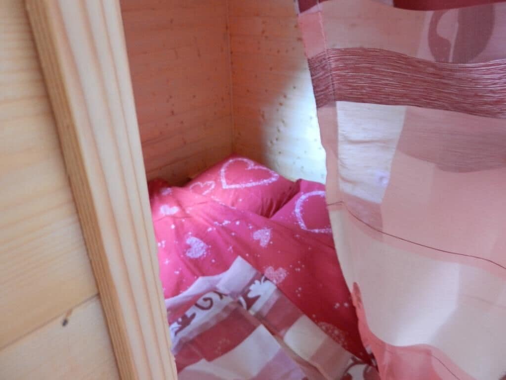 Una habitación pequeña y cerrada con una colcha rosa y un cabecero de madera.