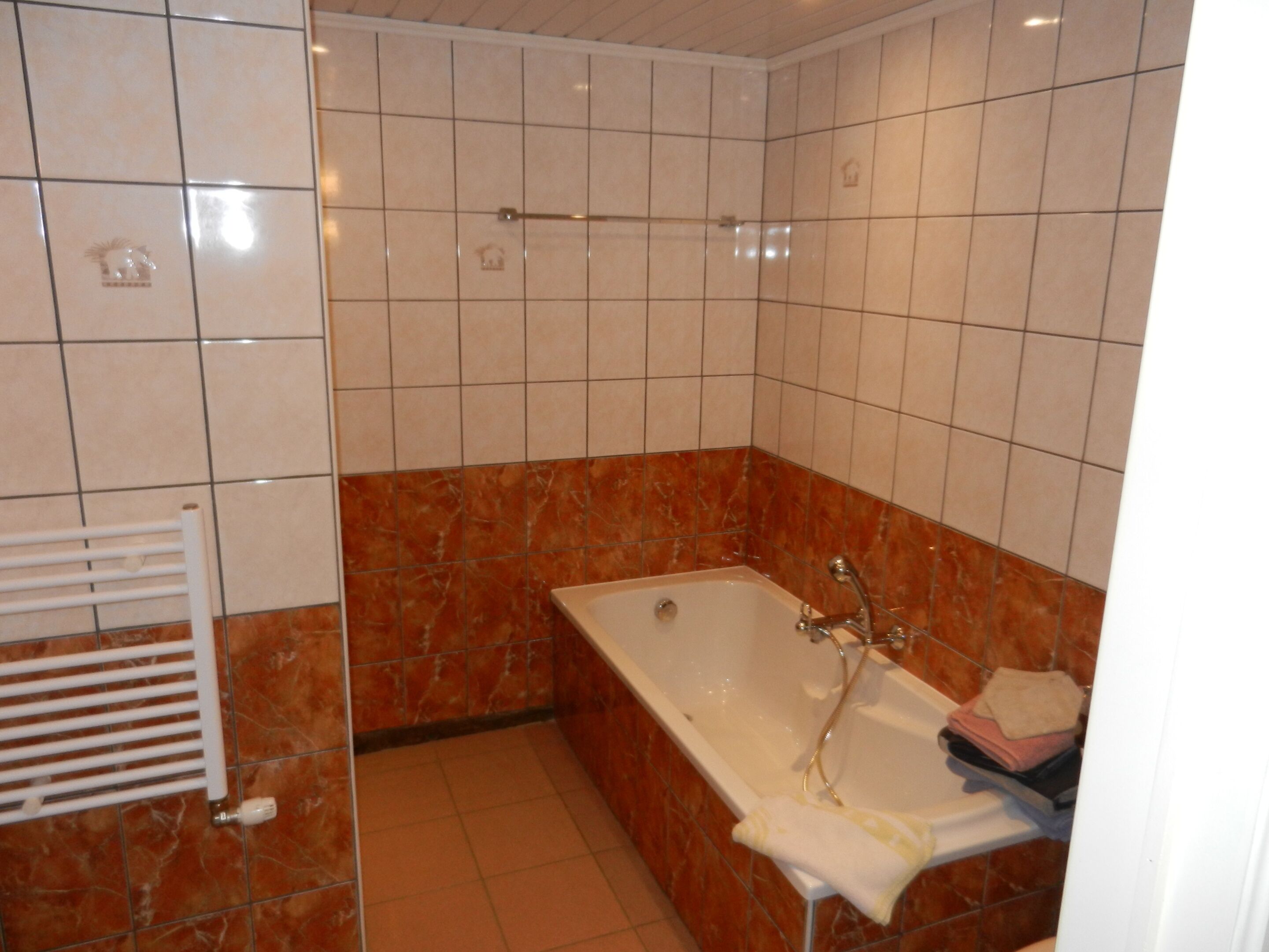 Een badkamer met een bad, een handdoekhouder en een betegelde vloer.