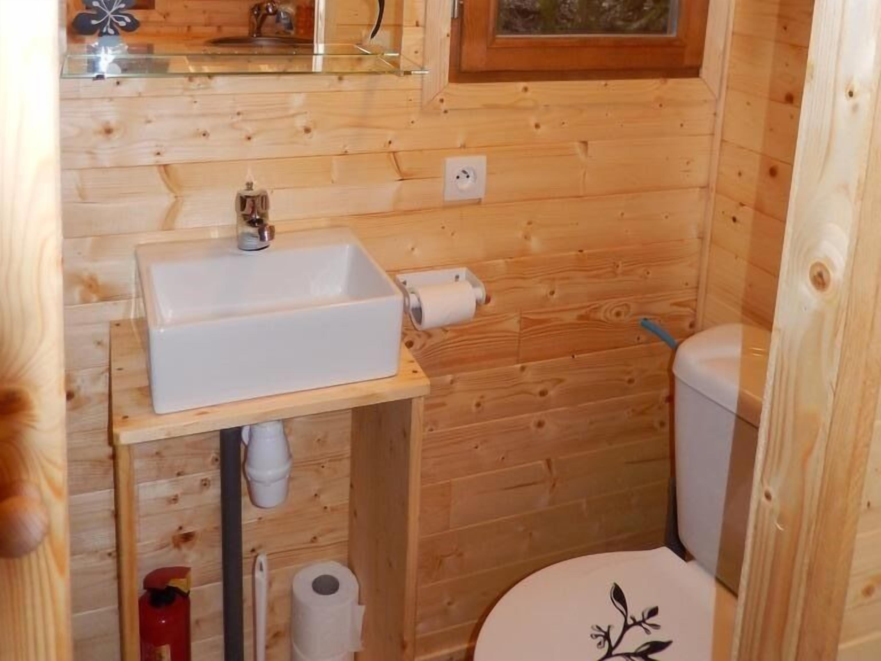 Un baño pequeño de madera con un lavamanos blanco, un inodoro y un espejo sobre el lavamanos.