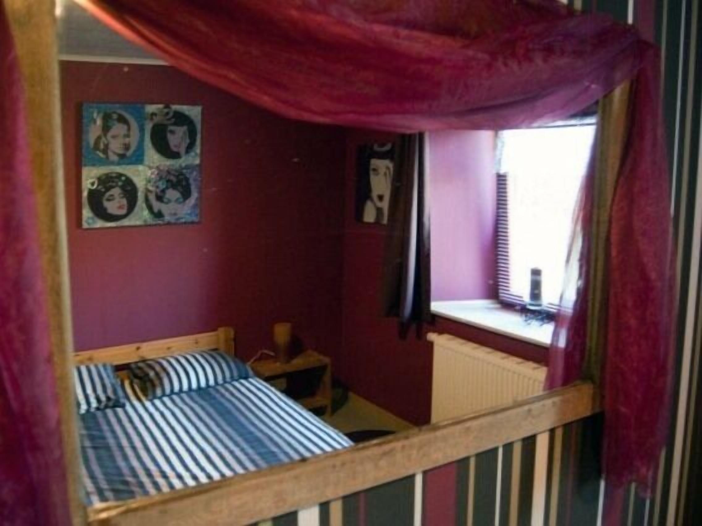 A bedroom with a bed, a window with blinds, a radiator, and a wall with a poster.