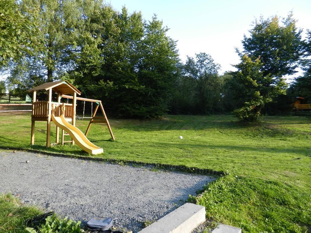 A playground with a wooden slide and swing set, surrounded by a grassy area and trees.