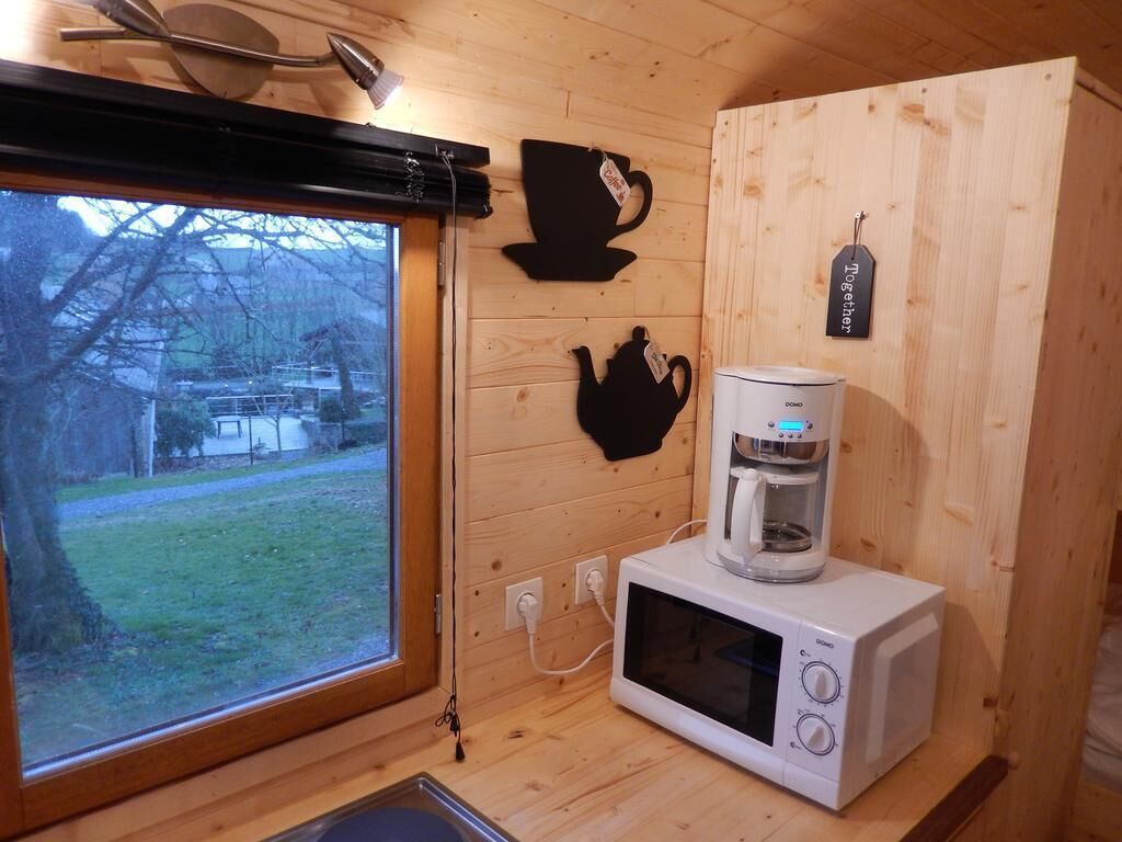A compact kitchen with a microwave and coffee maker, wooden walls, and a window with a view of a house and trees.