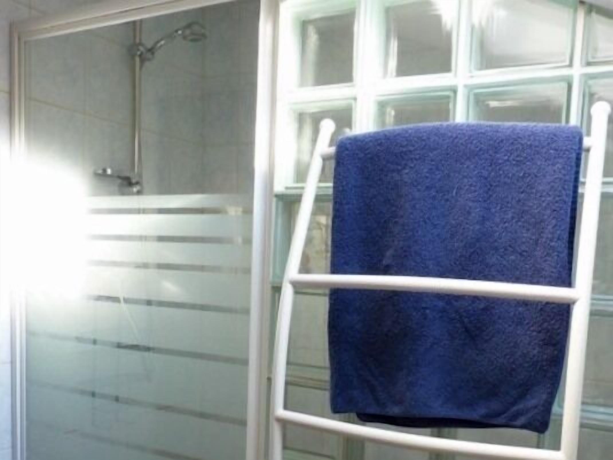 A bathroom with a glass shower enclosure, a white towel rack, and a blue towel hanging on it.