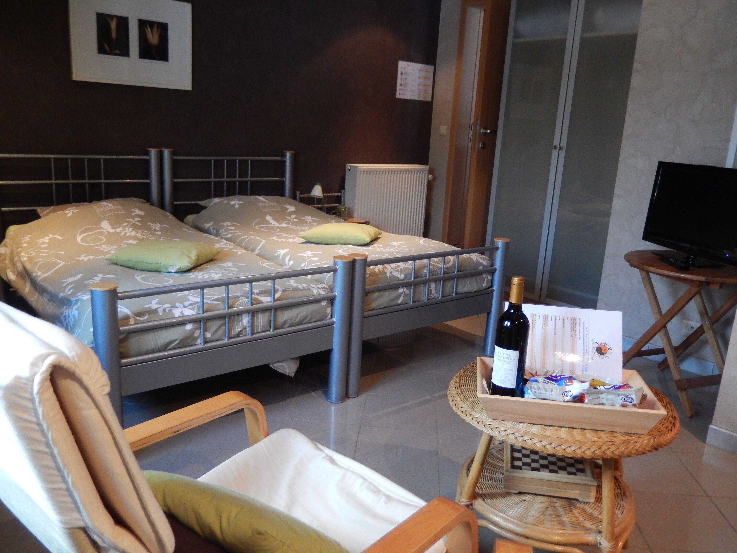 Een hotelkamer met een bed, een stoel, een tafeltje met een fles wijn en een televisie.