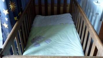 Una cuna de madera con un colchón verde y una cortina con estampado de estrellas.