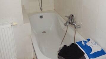 Een badkamer met een wit bad, een witte radiator en een handdoekrek met opgevouwen handdoeken.