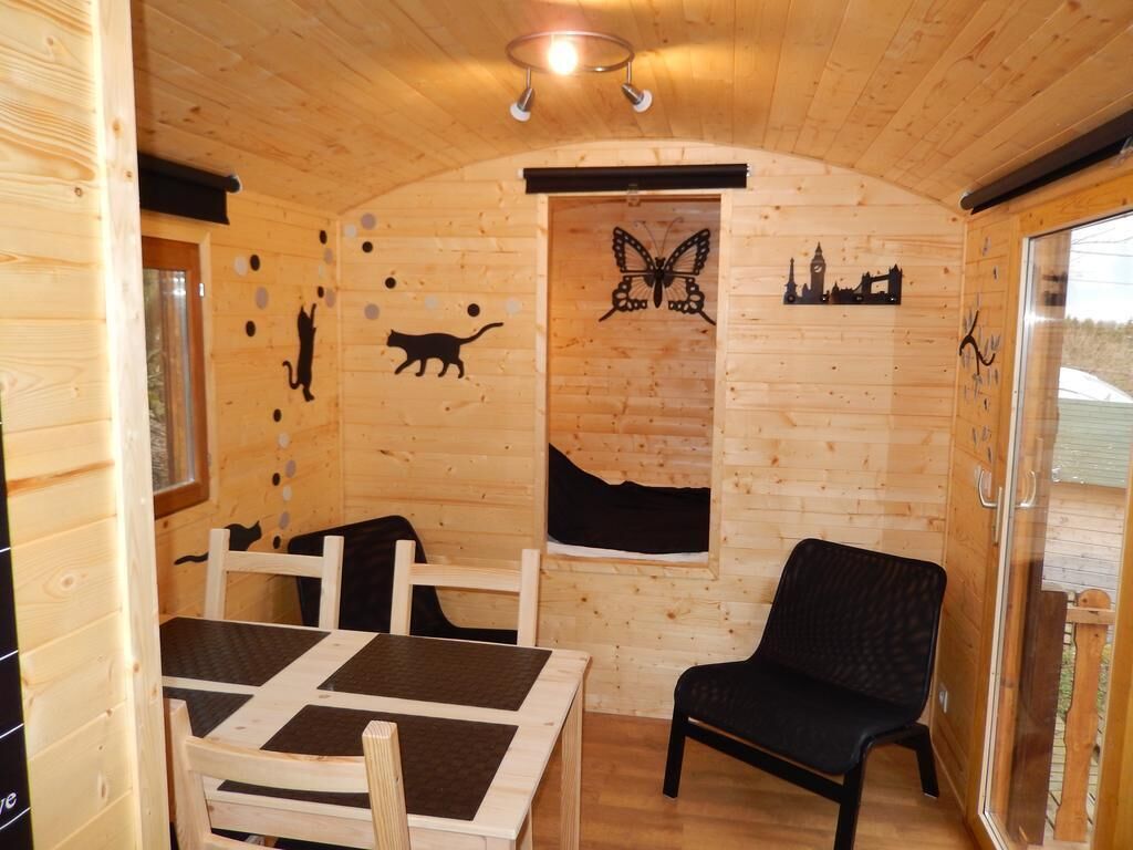 Interior acogedor de una cabaña de madera con una mesa y sillas, una silla negra, y adornos en la pared como siluetas de una mariposa y un gato.