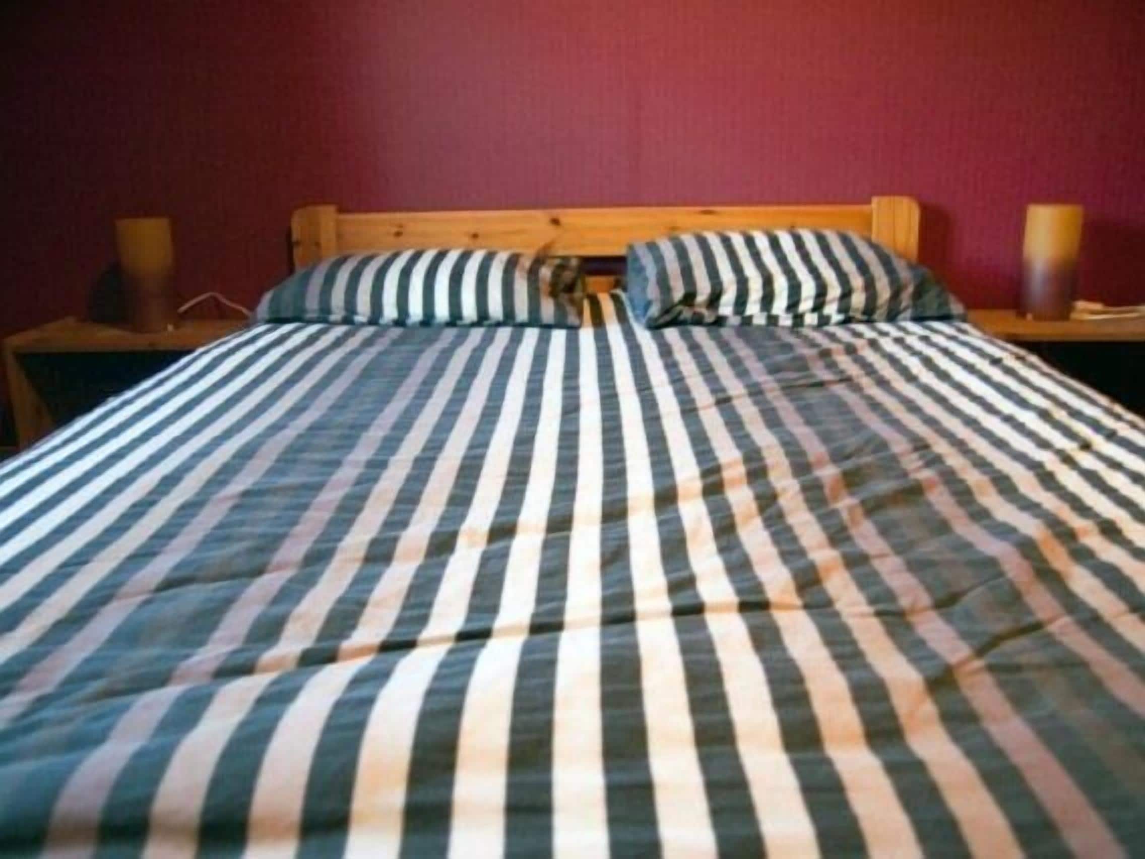 Ein Bett mit gestreiftem Bettbezug, einem hölzernen Kopfteil und zwei Nachttischlampen.