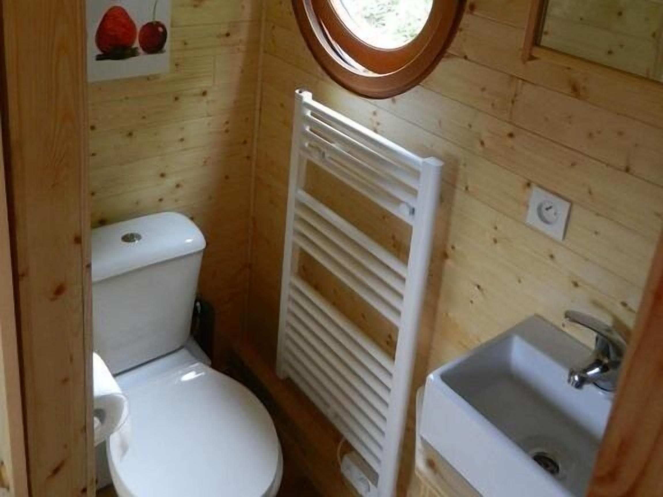 Ett litet badrum med träpanel, toalett, vitt handfat och handduksställ.