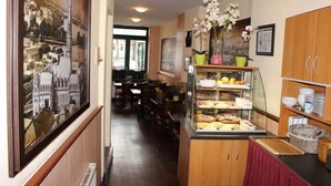 A hotel corridor with a café area featuring a glass display case with pastries and a view of the cityscape through a framed picture. - ALTAN Hotel (Hamburg)
